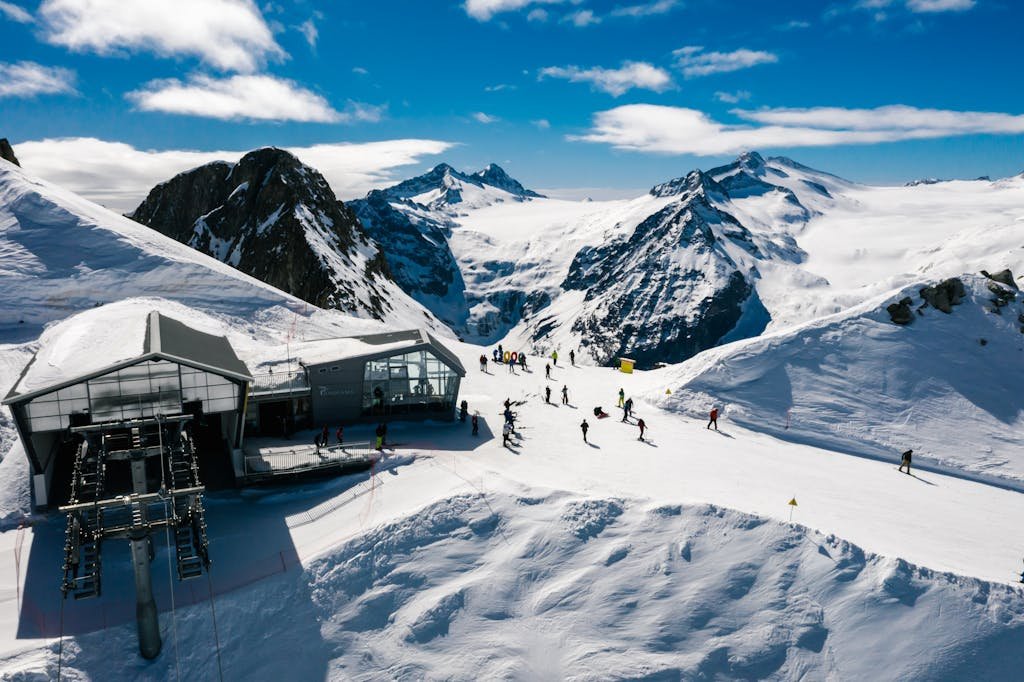 Scenic view of a ski resort with skiers, snowy mountains, and a ski lift under a clear blue sky.