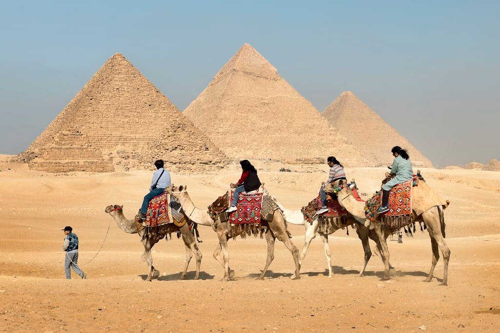 Tourists riding camels near the Great Pyramids of Giza, Egypt under clear skies.