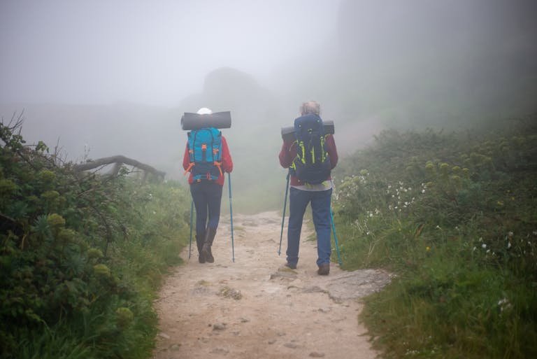 A couple enjoys a hiking adventure on a foggy trail in Portugal, surrounded by lush greenery. - Camino de Santiago