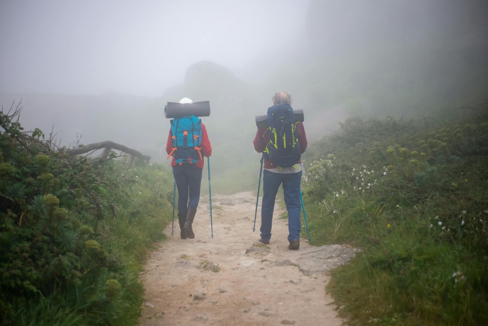 A couple enjoys a hiking adventure on a foggy trail in Portugal, surrounded by lush greenery. - Camino de Santiago
