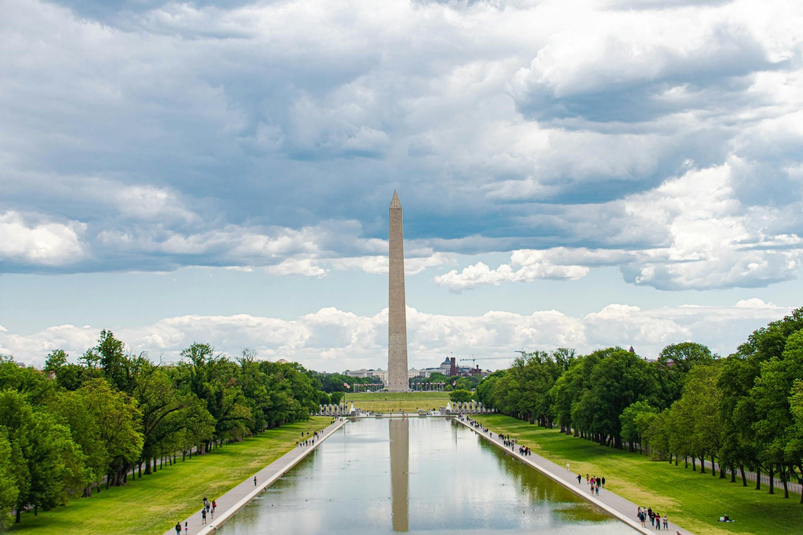 A scenic view of the Washington Monument in Washington, D.C., with reflections in the reflecting pool and a cloudy sky overhead.