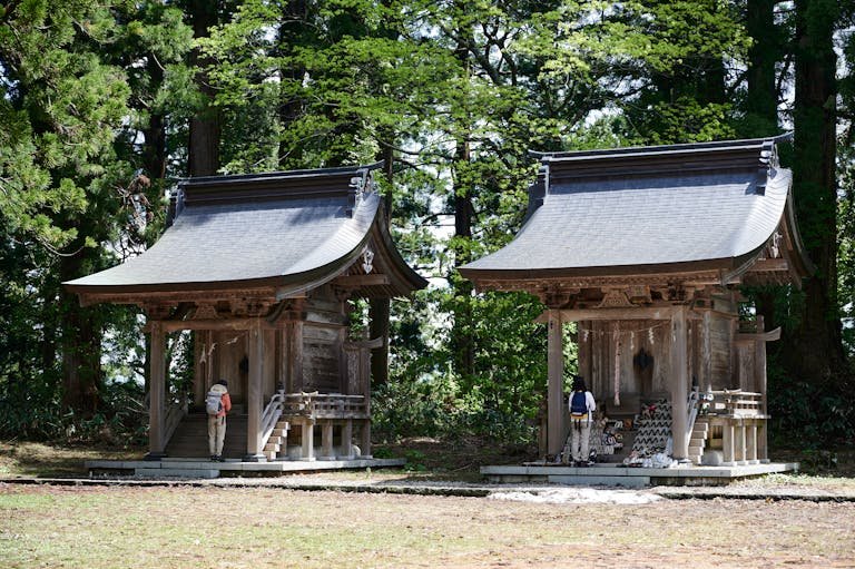 Backpackers visiting traditional shrines in a forest in Tsuruoka, Japan, embracing spirituality.