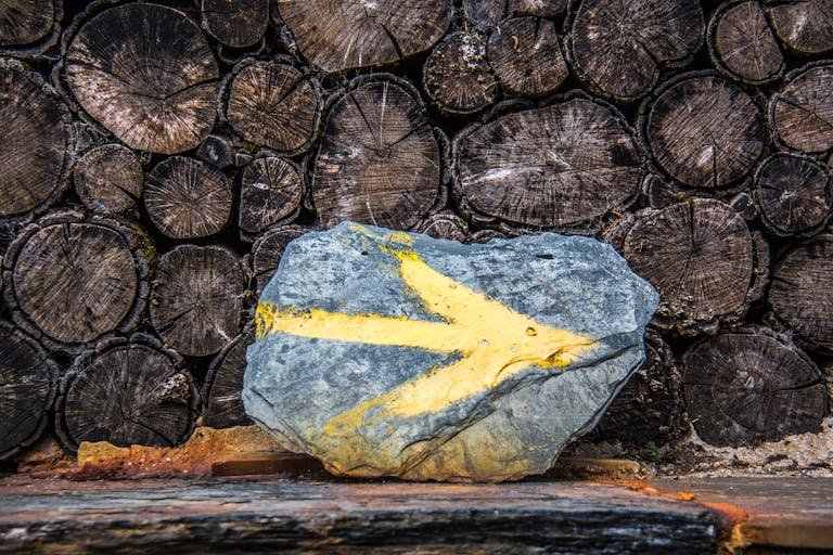 Close-up of a painted rock with a yellow arrow placed before a stacked timber backdrop.