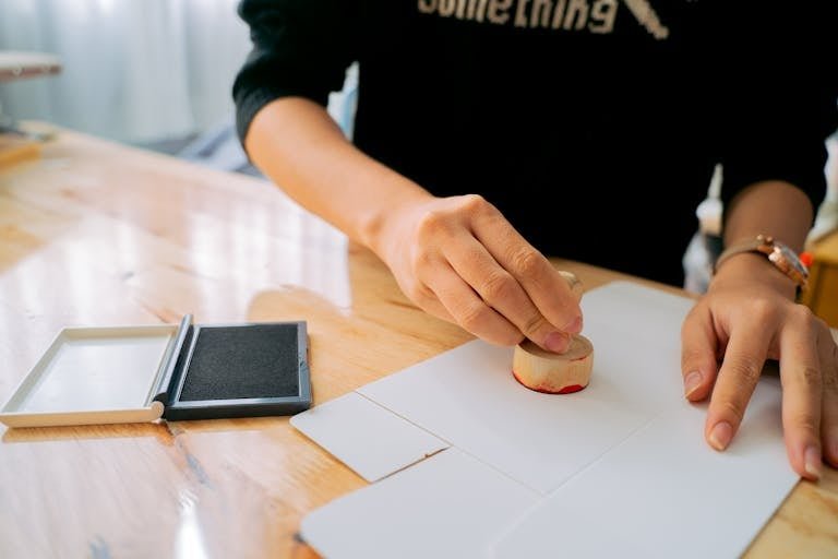 Close-up of hands stamping a document on a wooden desk indoors.
