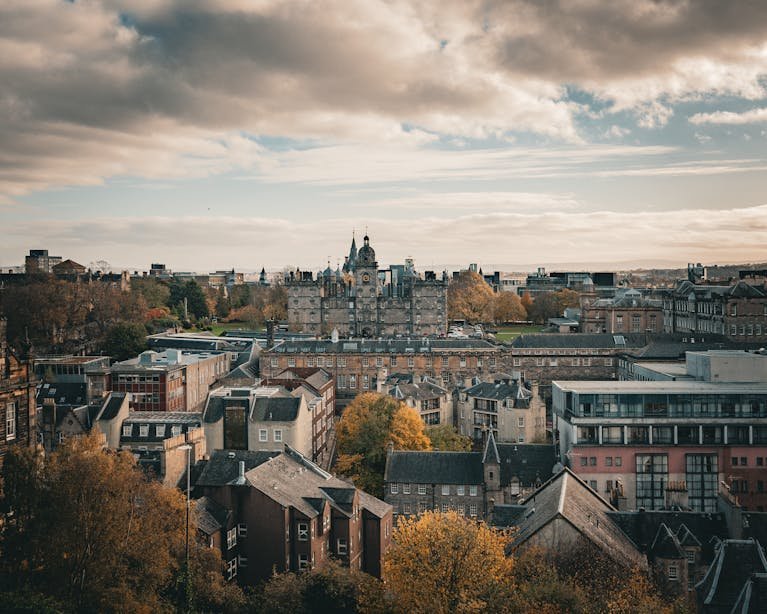 Stunning panoramic view of Edinburgh cityscape with autumn foliage and historic architecture.