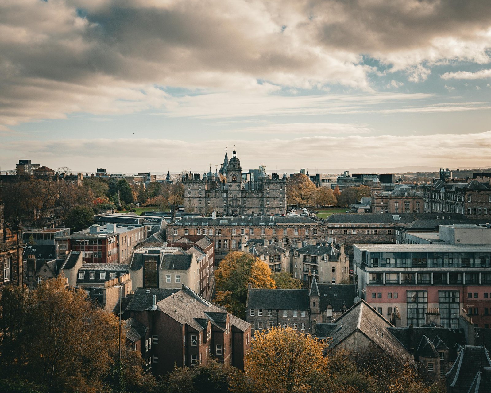 Stunning panoramic view of Edinburgh cityscape with autumn foliage and historic architecture.