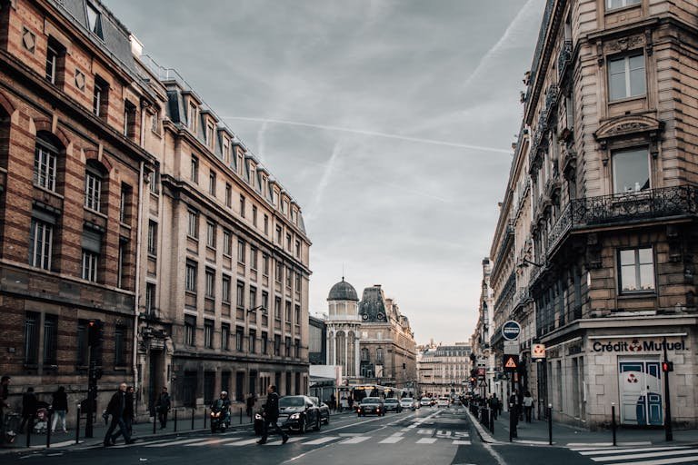 Urban street scene in Paris with classic architecture, cars, and pedestrians on an overcast day.