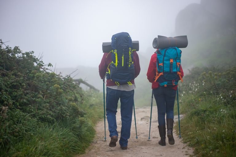 Hiking Poles: Worth the Hype? 4 A couple with backpacks and trekking poles hiking through a misty path in Portugal.