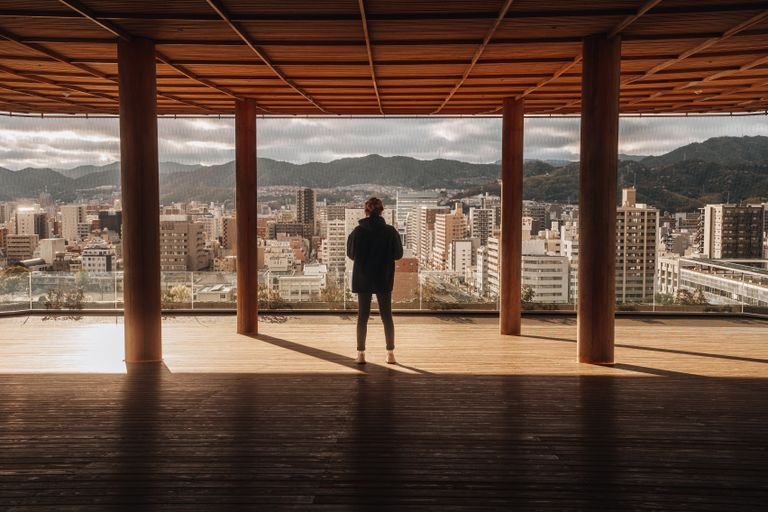 A person enjoys a panoramic city view of Hiroshima from a modern terrace.