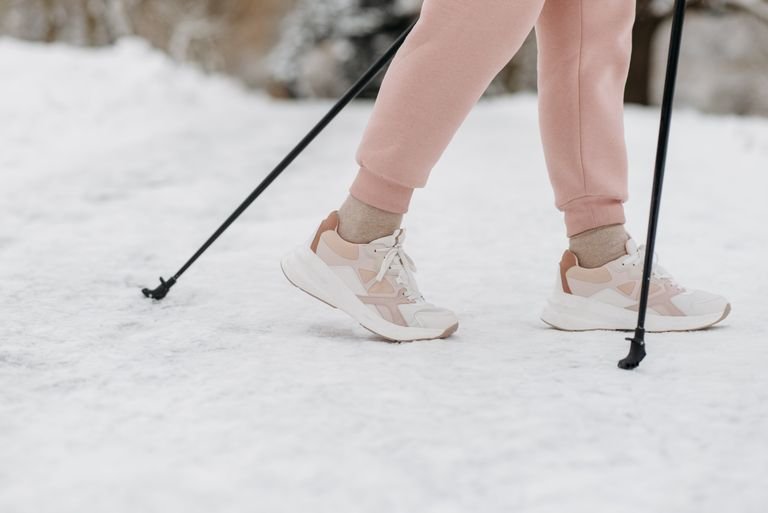 A person wearing sneakers and pink pants walking with poles on snow-covered ground in winter.
