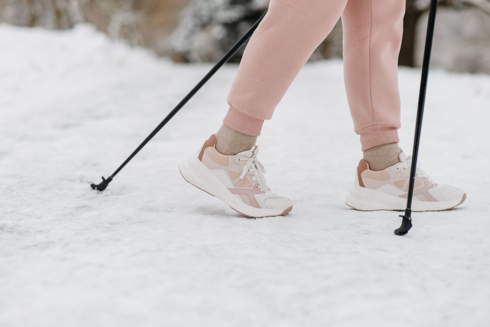 A person wearing sneakers and pink pants walking with poles on snow-covered ground in winter.
