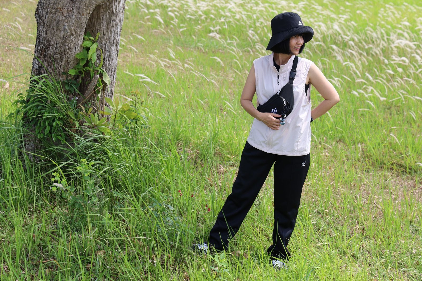 An Asian woman stands in a meadow wearing stylish attire, embodying fashion and tranquility.