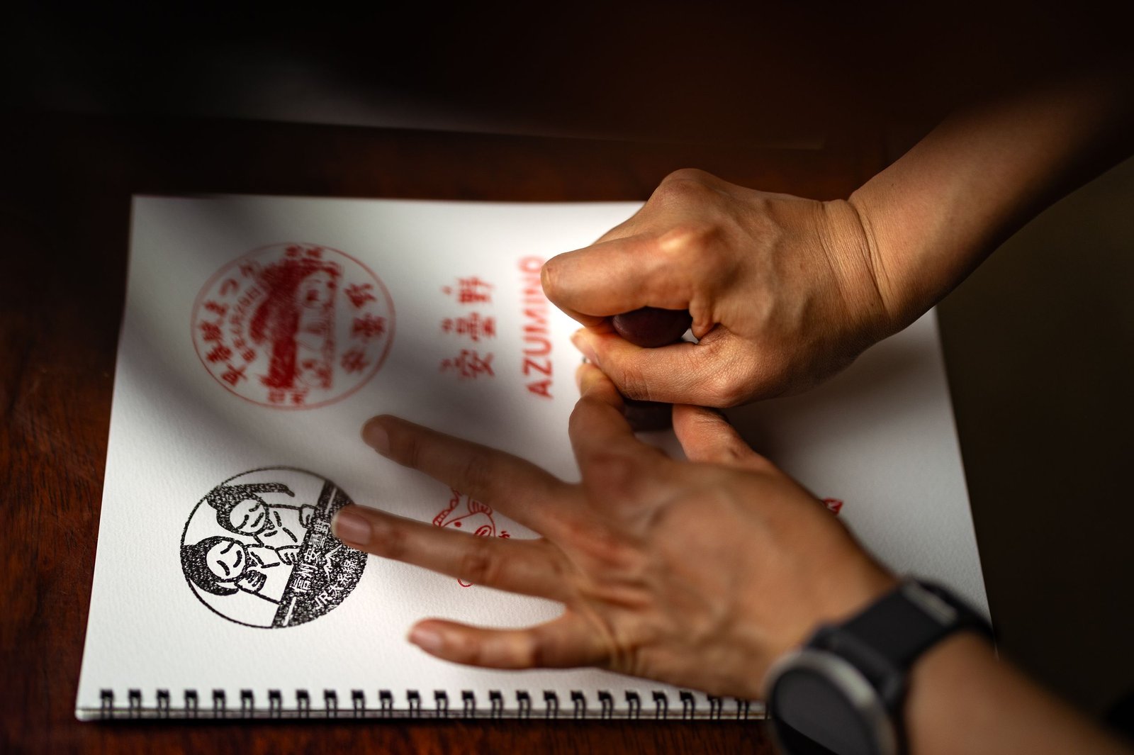 Hands stamping intricate designs in a sketchbook, showcasing artistic precision.
