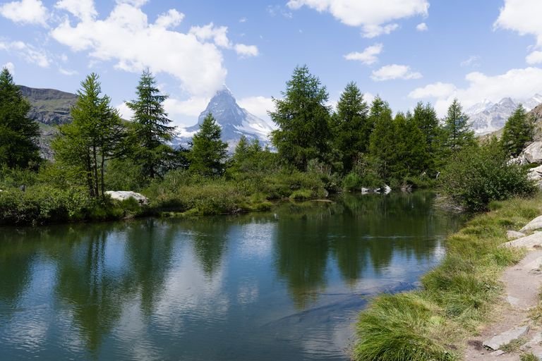 Picturesque image of the Matterhorn peak reflecting in a serene alpine lake surrounded by lush greenery.