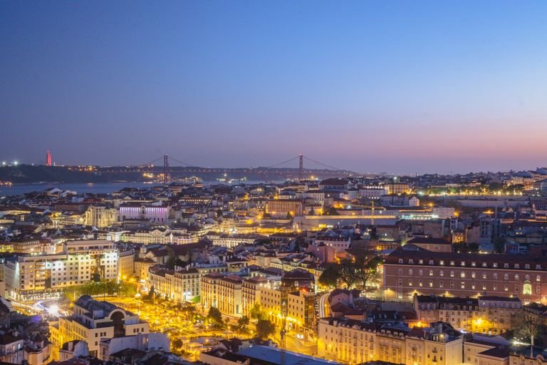 Scenic view of Lisbon cityscape at twilight, featuring lights, skyline, and historic architecture.